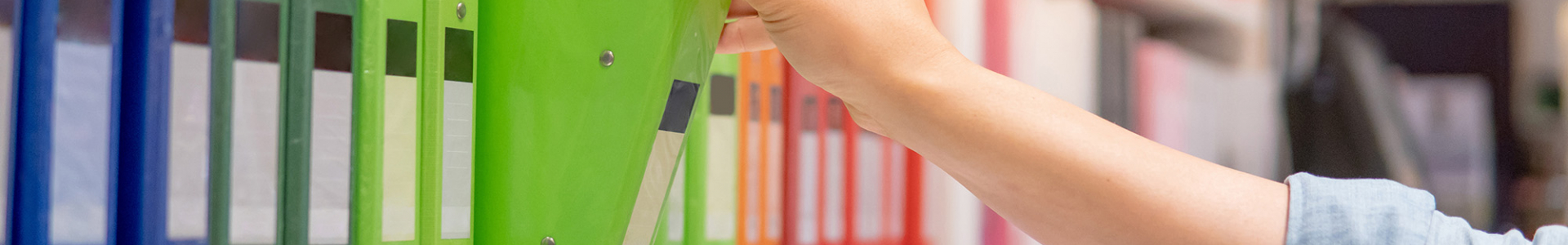 photo of someone grabbing a green binder off a shelf amidst other colorful binders