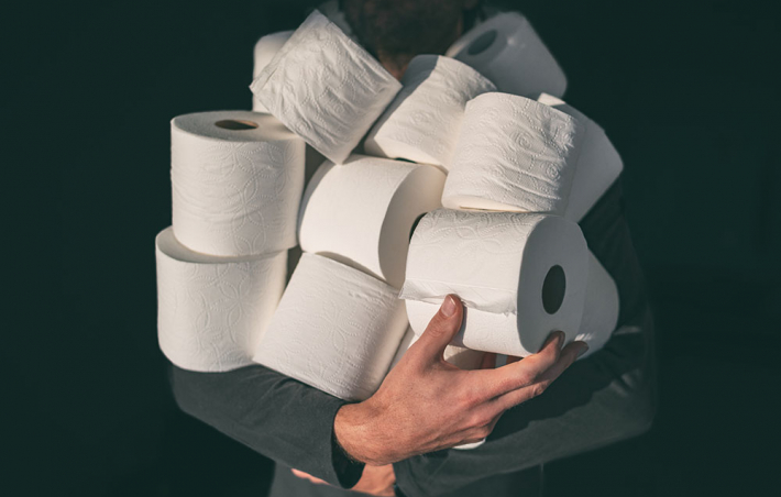 photo of someone holding a bunch of toilet paper rolls in their arms. their face is hidden behind the mound of tp